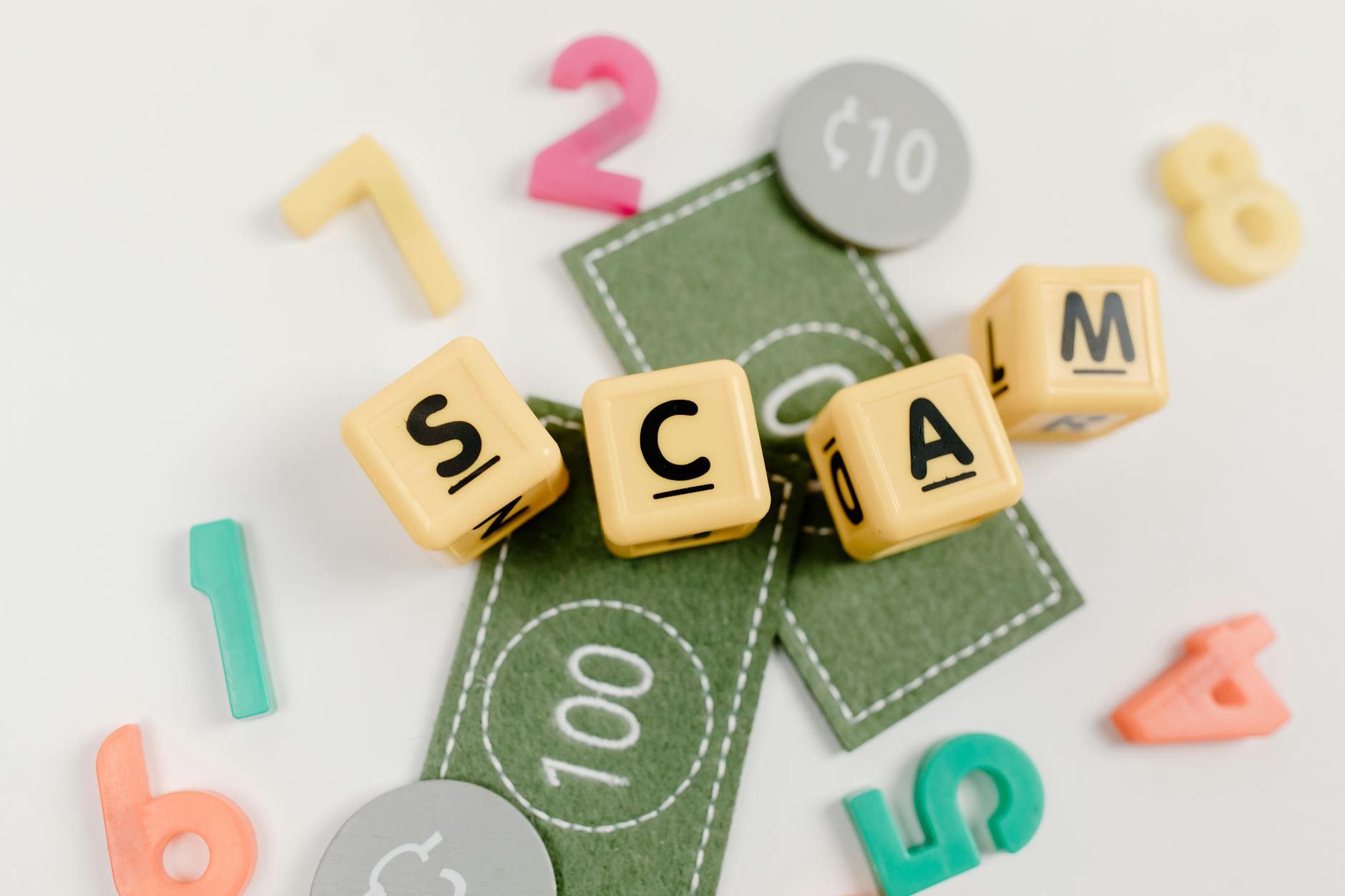 Scrabble letters spelling 'SCAM' surrounded by play currency and coins, symbolizing real estate fraud.